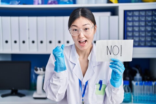 Chinese young woman working at scientist laboratory holding no banner screaming proud, celebrating victory and success very excited with raised arms