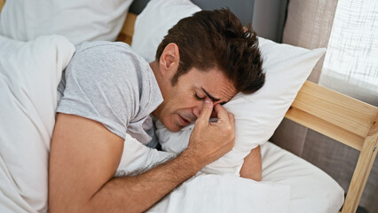 Young hispanic man lying on bed with sad expression crying at bedroom