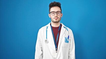 Young hispanic man doctor standing with serious expression over isolated blue background