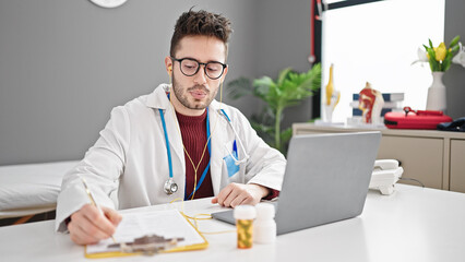 Fototapeta premium Young hispanic man doctor on video call prescribe pills writing clipboard at clinic