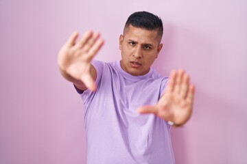Young hispanic man standing over pink background doing frame using hands palms and fingers, camera perspective