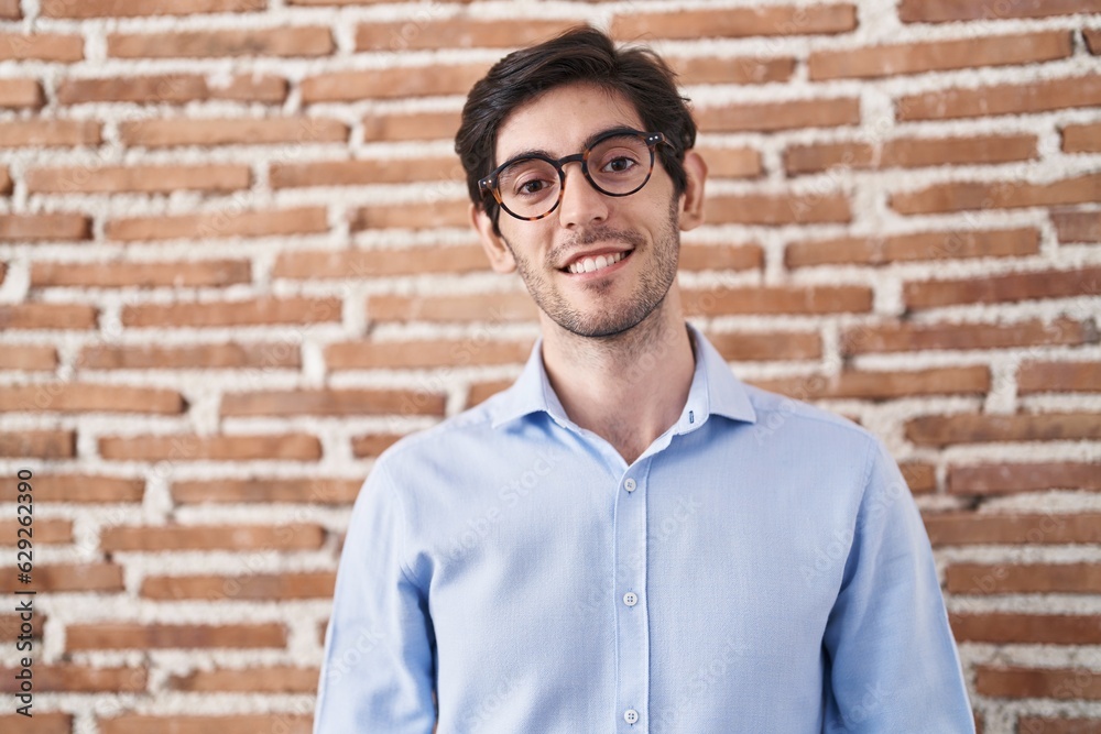 Canvas Prints Young hispanic man standing over brick wall background with hands together and crossed fingers smiling relaxed and cheerful. success and optimistic