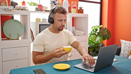 Young man using laptop and headphones drinking coffee at dinning room