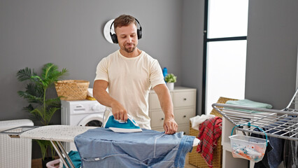 Young man listening to music ironing clothes at laundry room