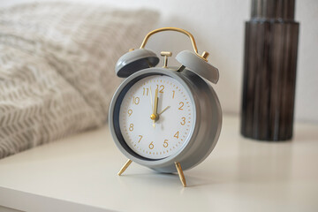Retro alarm clock stands on a white bedside table near the bed