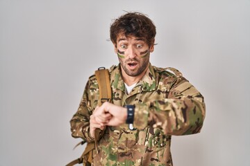 Hispanic young man wearing camouflage army uniform looking at the watch time worried, afraid of getting late