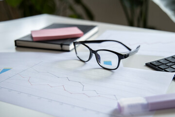 Lots of charts, diary, keyboard, glasses on the desktop. Top view, flat lay