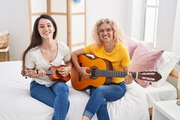 Two women mother and daughter playing classical guitar and ukulele at bedroom