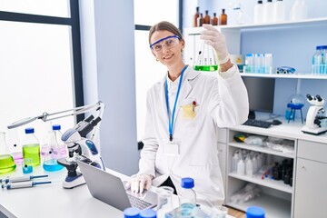 Fototapeta na wymiar Young caucasian woman scientist holding test tube using laptop at laboratory
