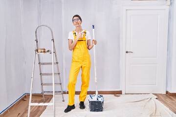 Young caucasian woman painting walls pointing aside worried and nervous with forefinger, concerned...
