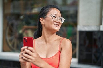 Young chinese woman smiling confident using smartphone at street
