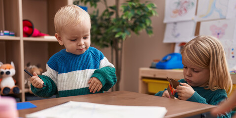 Adorable boy and girl student cutting paper sitting on table at kindergarten