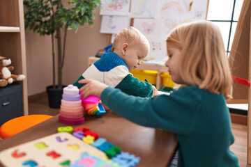 Adorable boy and girl playing with construction blocks sitting on table at kindergarten