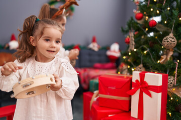 Two kids wearing reindeer ears decorating christmas tree at home