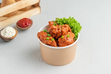 Closeup of a white cup with buffalo wings with greens