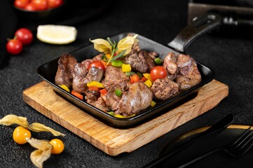 Black pan with chicken liver, cherry tomato, and chopped capsicum.