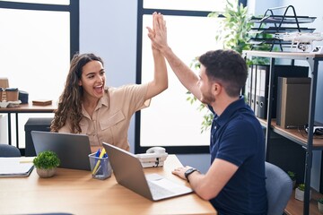 Young hispanic couple business workers high five with hands raised up working at office