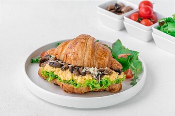 Croissant sandwich with mushrooms and lettuce on a white plate