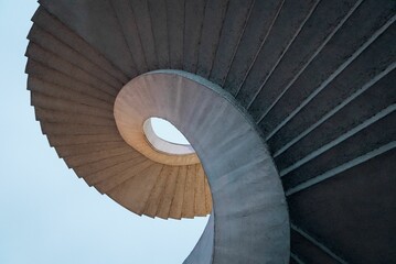 Low angle shot of curved spiral stairs under a bright blue sky - obrazy, fototapety, plakaty