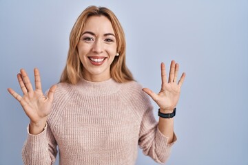 Hispanic woman standing over blue background showing and pointing up with fingers number ten while smiling confident and happy.