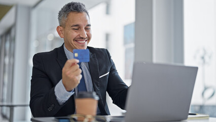 Young hispanic man business worker using laptop holding credit card at office