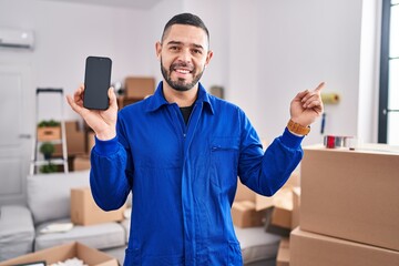 Hispanic man working on moving service showing smartphone screen smiling happy pointing with hand and finger to the side