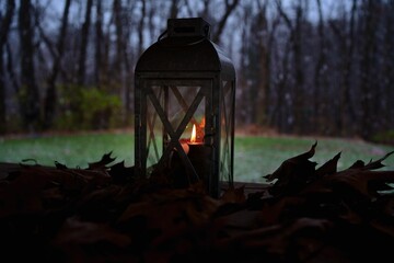 Vintage lantern with a burning candle inside on a wooden surface with fallen autumn leaves