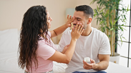 Man and woman couple sitting on bed applying facial skin treatment at bedroom