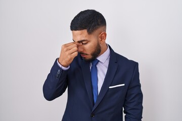 Young hispanic man wearing business suit and tie tired rubbing nose and eyes feeling fatigue and headache. stress and frustration concept.