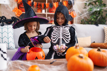 Adorable boy and girl having halloween party putting candies in pumpkin basket at home