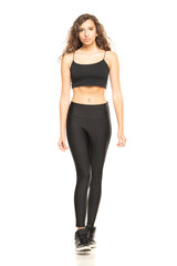 Fototapeta premium Young curly brunette posing in black leggings and shirt on a white background