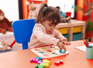 Fototapeta na wymiar Adorable hispanic girl playing with maths puzzle game sitting on table at kindergarten