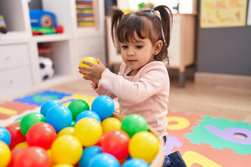 Fototapeta na wymiar Adorable hispanic girl playing with balls sitting on floor at kindergarten