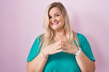 Caucasian plus size woman standing over pink background hands together and fingers crossed smiling relaxed and cheerful. success and optimistic