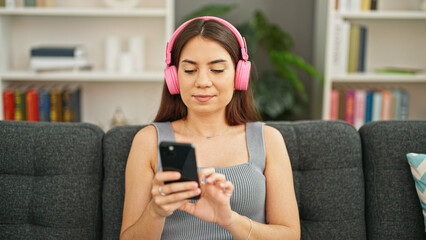 Young beautiful hispanic woman listening to music sitting on sofa at home