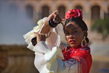 Young black and South American woman in a beige gypsy flamenco suit and red shawl, dancing with...