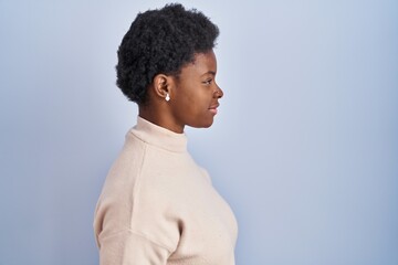 African american woman standing over blue background looking to side, relax profile pose with...