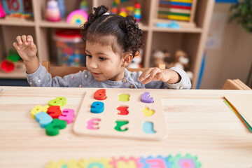 Fototapeta premium Adorable hispanic girl playing with maths puzzle game sitting on table at kindergarten