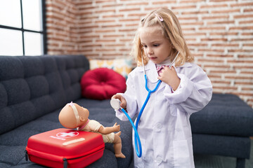 Adorable blonde girl playing doctor with baby doll at home