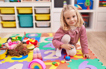 Adorable blonde girl playing with hoops game sitting on floor at kindergarten