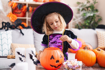 Adorable blonde girl wearing witch costume holding sweets on pumpkin basket at home