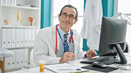 Middle age man doctor using computer smiling at the clinic