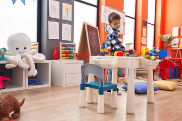Adorable caucasian boy playing with construction blocks standing at kindergarten