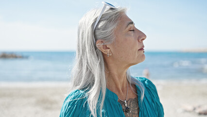 Fototapeta na wymiar Middle age grey-haired woman smiling confident breathing at beach