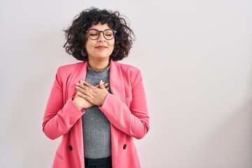 Hispanic woman with curly hair standing over isolated background smiling with hands on chest with closed eyes and grateful gesture on face. health concept.