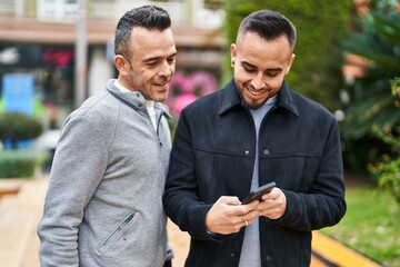 Two men couple smiling confident using smartphone at park