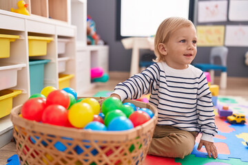 Obraz premium Adorable caucasian boy playing with balls sitting on floor at kindergarten