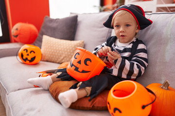 Adorable caucasian boy wearing pirate costume holding sweet on pumpkin basket at home