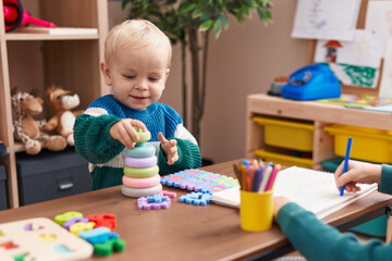 Adorable caucasian boy playing with toys sitting on table at kindergarten