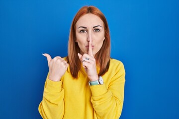 Young woman standing over blue background asking to be quiet with finger on lips pointing with hand to the side. silence and secret concept.